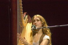 a woman with long hair holding a large instrument in front of a microphone on stage