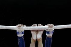 the legs and feet of an individual performing on parallel bars, with their hands in the air