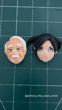 two doll heads are sitting on top of a green surface, one has an old man's face and the other is a woman's head