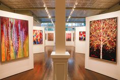 an art gallery with paintings on the walls and wooden floors, along with white pedestals