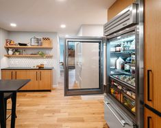 an open refrigerator in a kitchen with wooden cabinets and shelves on the wall, next to a counter