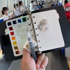 a person holding a notebook with a drawing on it and some markers in front of them