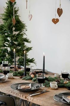 the table is set for christmas dinner with candles and ornaments hanging from the tree in the background