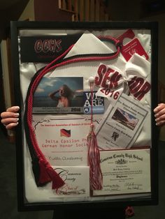 a person holding up a framed poster with various items attached to the back of it