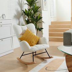 a white rocking chair sitting next to a glass table with a yellow pillow on it