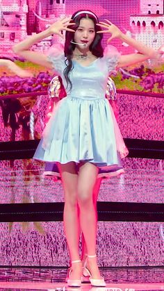 a woman in a short blue dress standing on stage with her hands behind her head