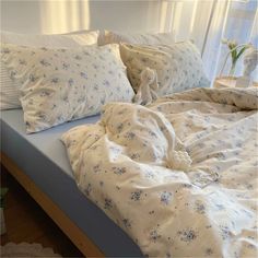 an unmade bed with white sheets and blue flowers on the comforter is in front of a window