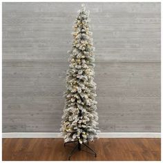 a white christmas tree with lights and snow on the branches in front of a wooden wall