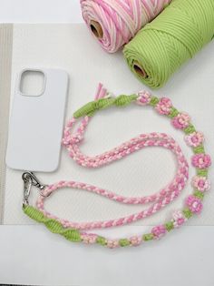 a pink and green lanyard next to two spools of yarn on a white surface