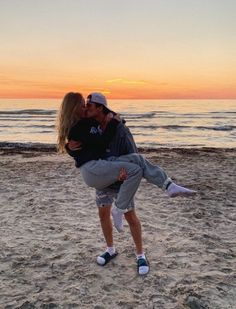 a man and woman kissing on the beach at sunset with water in the back ground