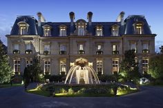 a large building with a fountain in front of it at night, surrounded by greenery and trees