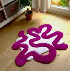 a pink and white rug on the floor in front of a window with a potted plant