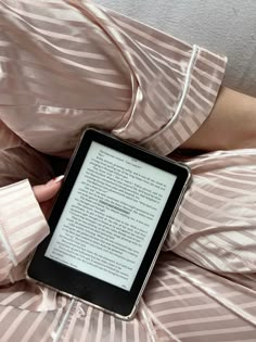 a woman laying on her stomach holding an electronic device in her hand and reading it