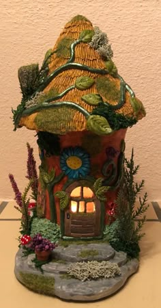 a small house made out of clay with plants and flowers on the roof is lit up