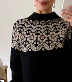 a woman holding up a cell phone in front of her face and wearing a black sweater