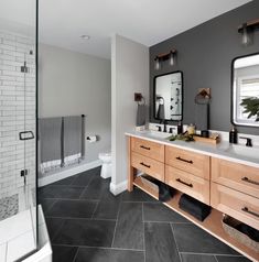 a bathroom with gray walls and black tile flooring, two large mirrors on the wall