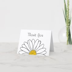 a thank you card with a daisy in a vase on a marble countertop next to it