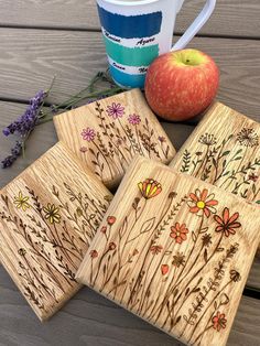 four wooden coasters with flowers on them next to an apple and flowery plant