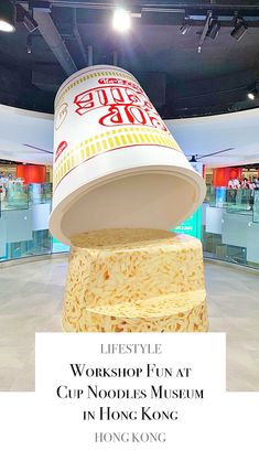 a large cup sitting on top of a pile of noodles in a building with the words,