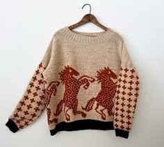 a sweater hanging on a hanger with two horses in red and white knits