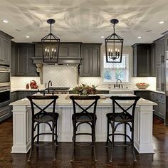 a kitchen with gray cabinets and white counter tops, two bar stools at the center