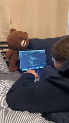 a person sitting on a bed with a laptop and a teddy bear in the background