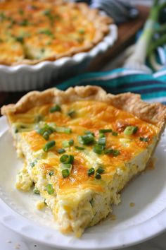 a slice of quiche on a plate with green onions and scallions in the background