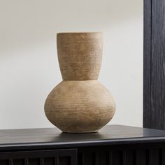 a brown vase sitting on top of a wooden table next to a black cabinet and white wall