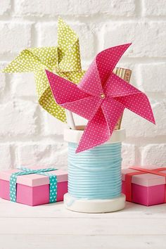 some paper flowers are in a vase on a white table with pink and blue boxes