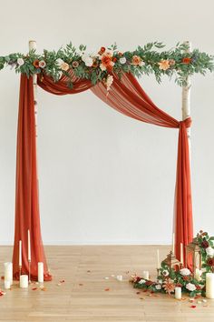 an orange and white wedding arch decorated with flowers, candles and greenery on the floor