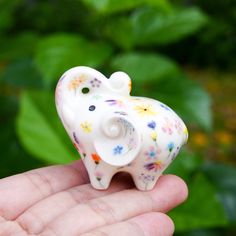 a small elephant figurine sitting on top of someone's hand in front of some plants