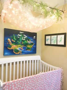 a baby's crib with a painting hanging on the wall and lights above it