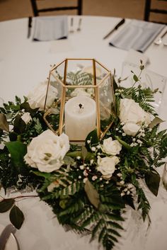 a candle and some flowers on a white table cloth at a wedding reception with greenery