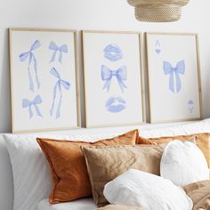 three blue and white prints on the wall above a bed with pillows, blankets and throw pillows