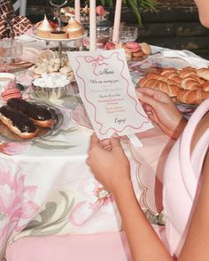 a woman sitting at a table covered in pastries and desserts with a menu