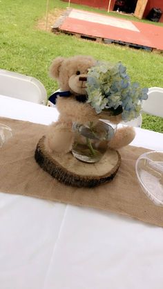 a teddy bear sitting on top of a piece of wood next to a vase filled with flowers