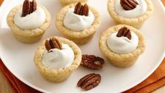 small pecan pies on a white plate topped with whipped cream and pecans