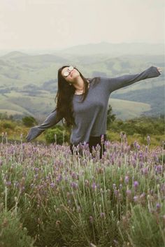 a woman standing in a field with her arms outstretched and eyes closed, wearing sunglasses