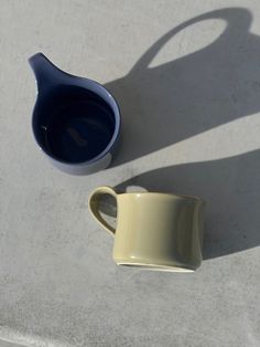 two mugs sitting next to each other on top of a cement surface with shadows