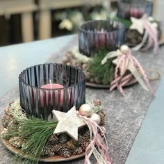 two candles are sitting on a table with pine cones