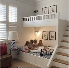 three children are sitting on their bed under the stairs in this room with white walls