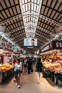 people are walking through an indoor market with lots of food on the tables and in front of them