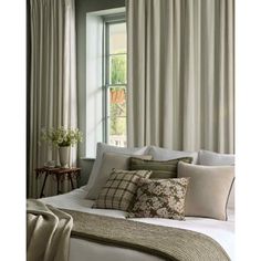 a white bed sitting under a window next to a green plant in a vase on top of a table