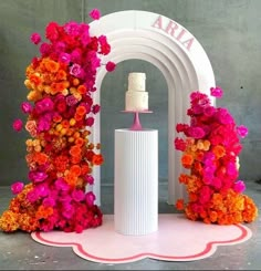 there is a cake on top of a white vase with flowers around it and an arch in the background