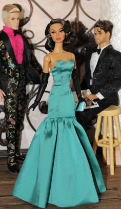 two dolls dressed in formal clothes and one is holding a purse while the other looks on