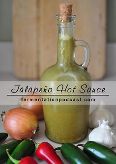 a bottle filled with green liquid next to some peppers and garlic on a white table