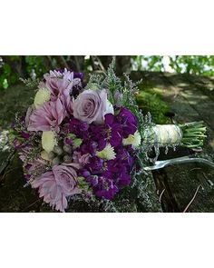 a bouquet of purple and white flowers sitting on top of a wooden table next to a tree