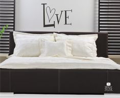 a bed with white sheets and pillows in front of a wall that says love on it