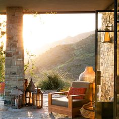 an outdoor living area with patio furniture and stone walls, overlooking the mountains at sunset