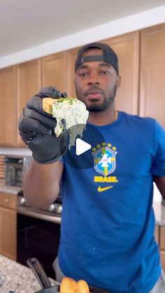 a man in a blue shirt and black gloves is holding up a piece of food